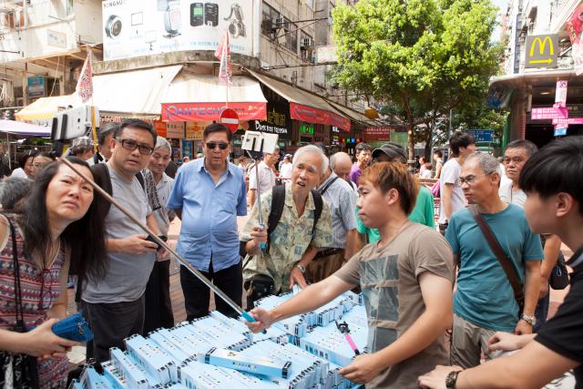 Vendor on Apliu street trying to convice a skeptical audience to buy his selfie-sticks